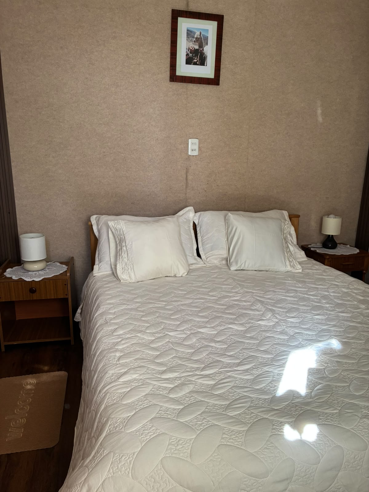 Cama matrimonial con cubrecama blanco y veladores de madera