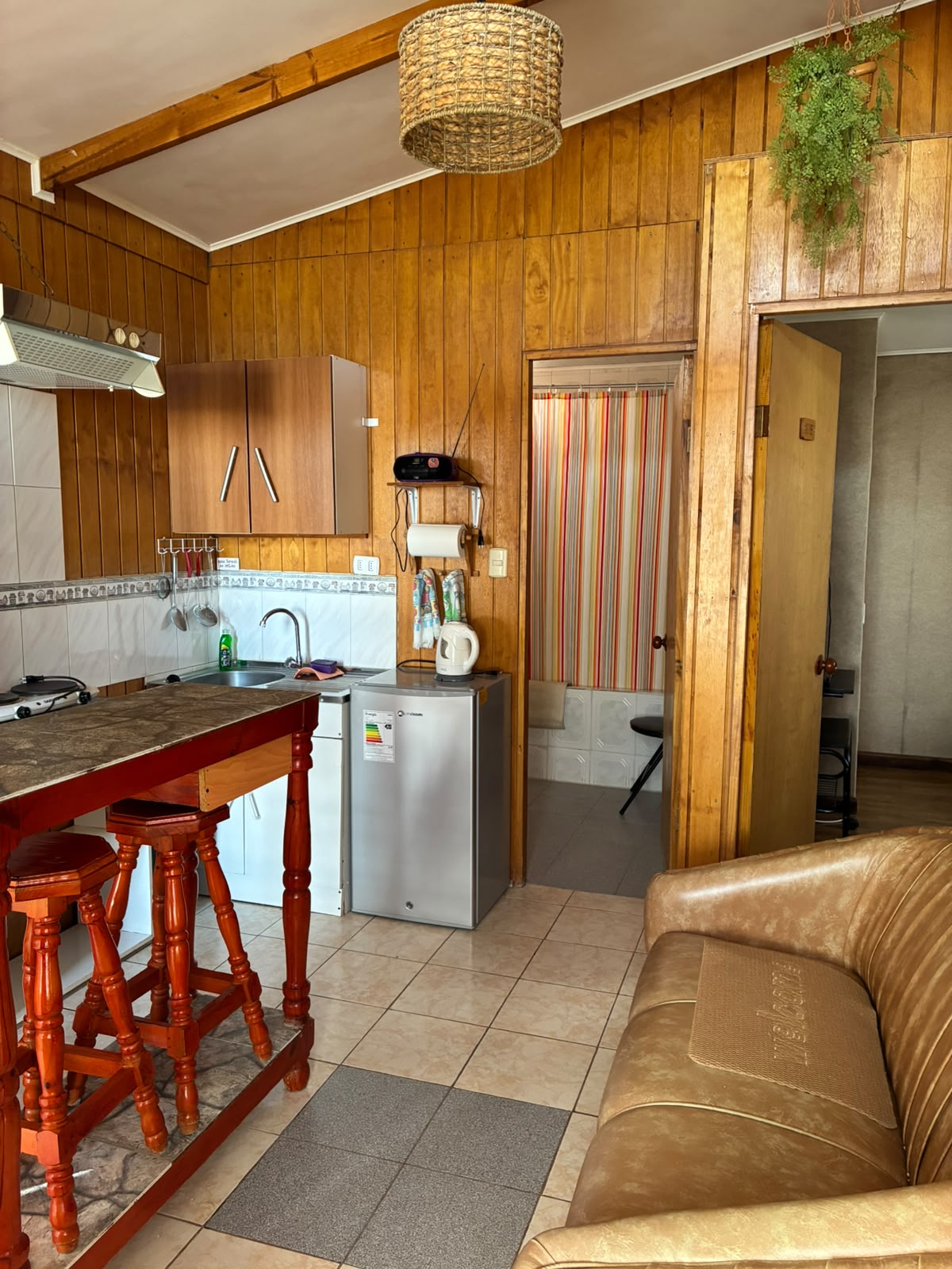 Interior de una cabaña con cocina, barra, refrigerador y sofá