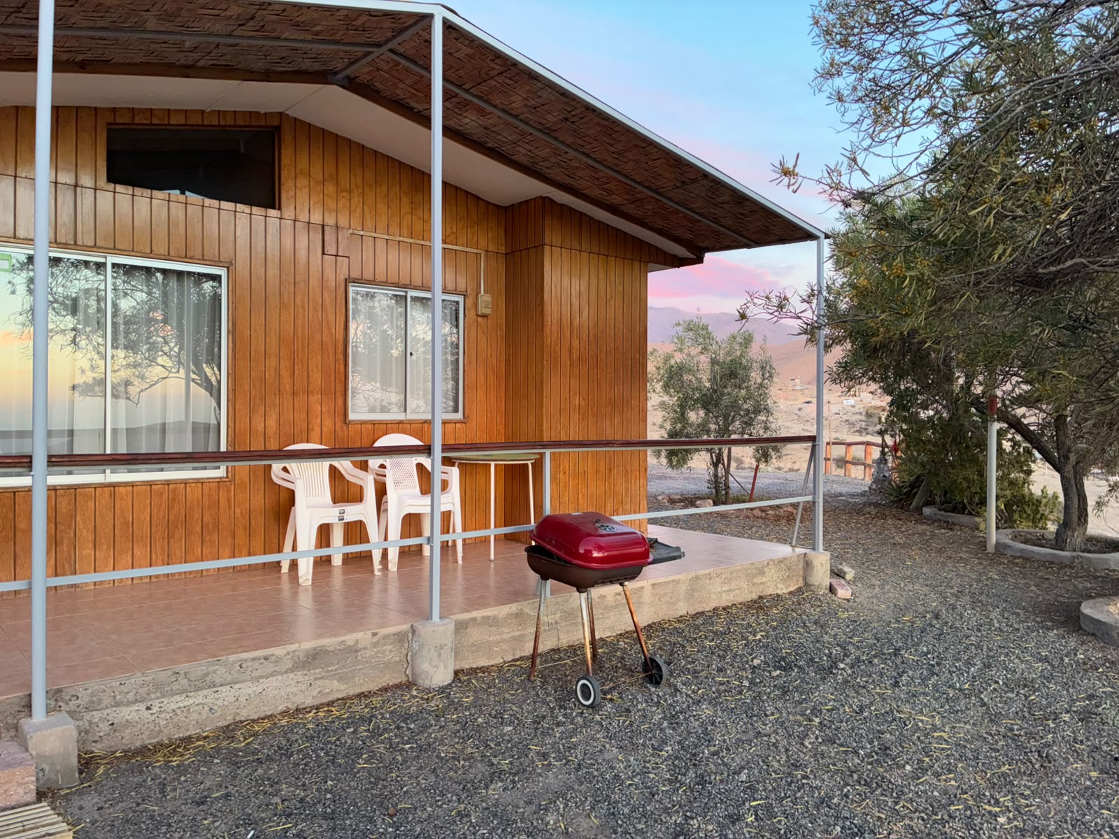 Terraza de una cabaña de madera con mesa, sillas y parrilla