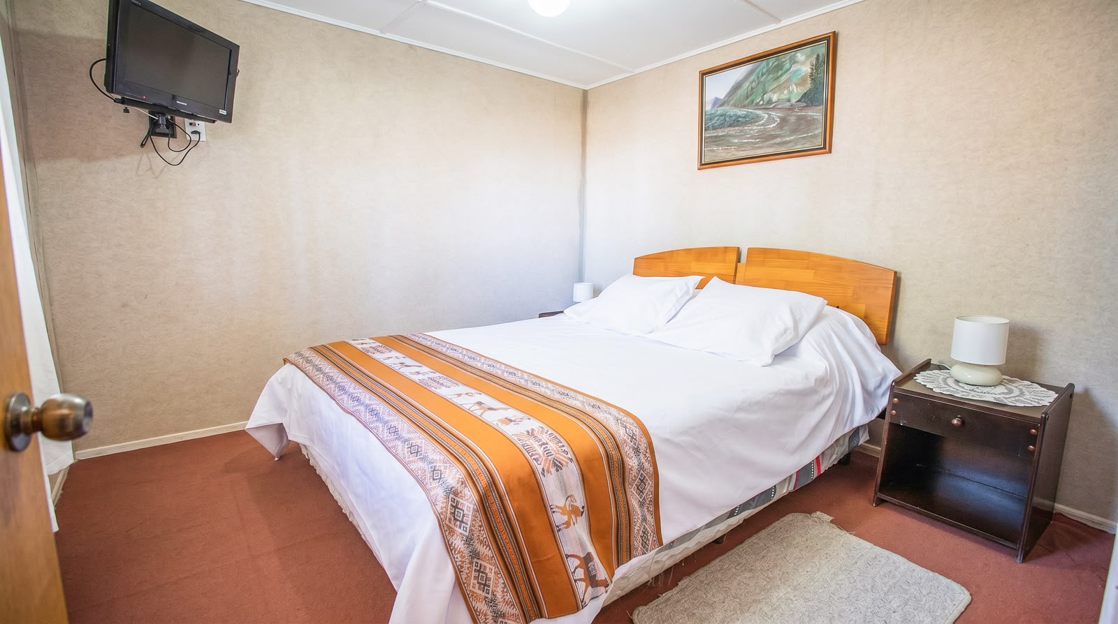 Habitación con cama matrimonial blanca y manta andina naranja