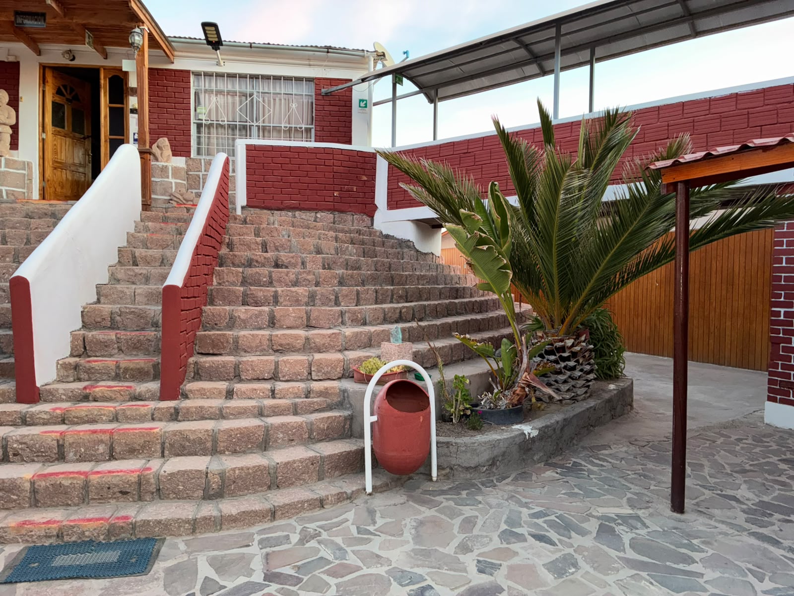 Patio del hotel con escalinatas de piedra, una palma y fachada roja y blanca