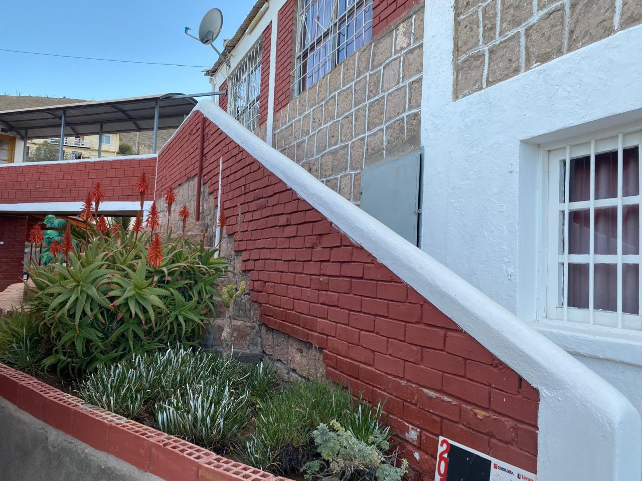 Fachada del hotel de piedra, rojo y blanco, con flores